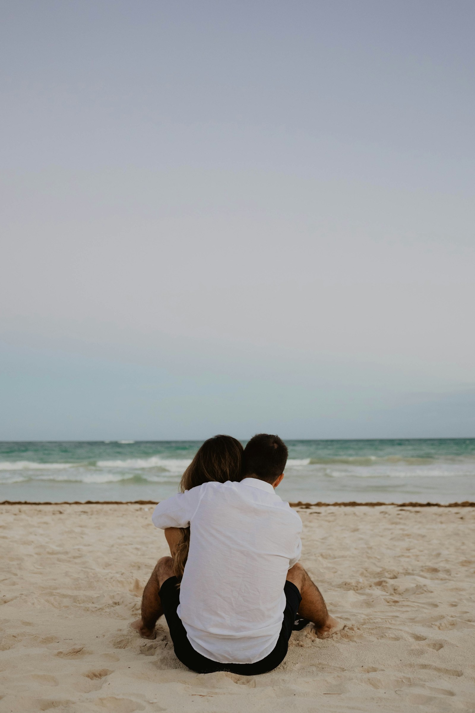 Two people sitting close together, looking towards the sea